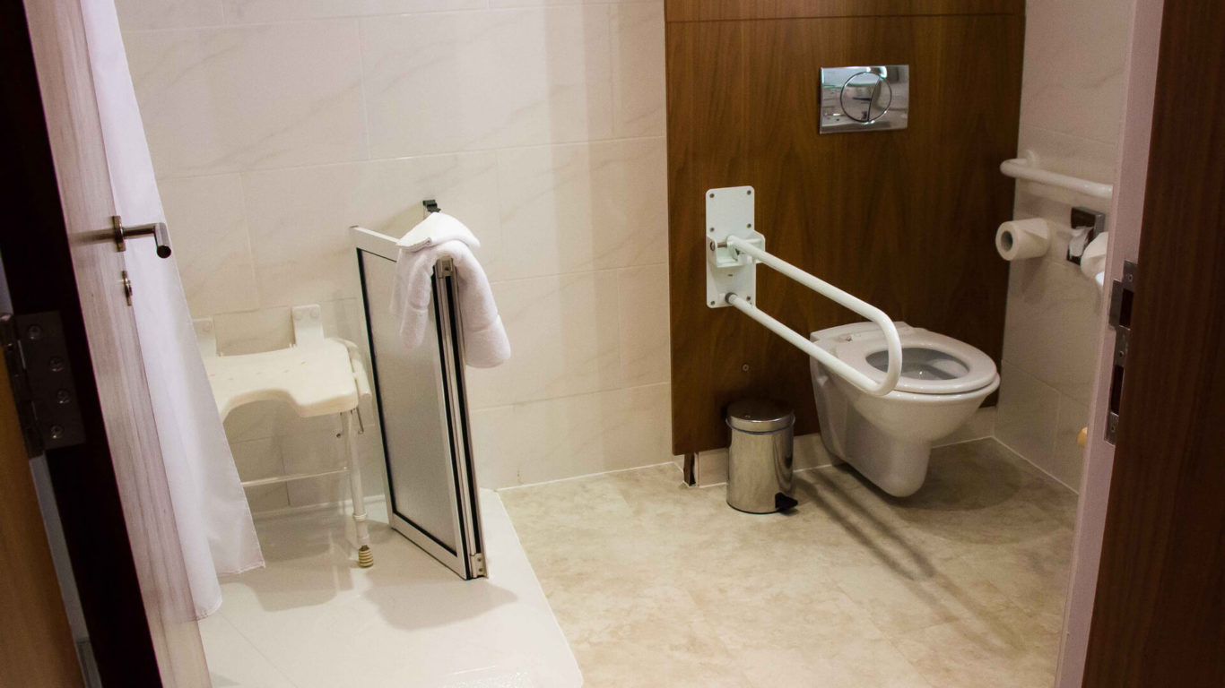 Modern hotel bathroom with accessible shower and toilet, featuring support bars and a comfortable bench for guest convenience.