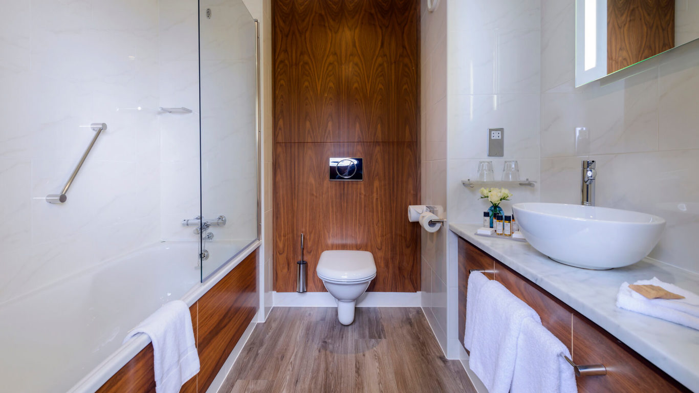 Luxurious hotel bathroom with marble sink, wooden accents, glass shower, fresh towels, and complimentary toiletries.