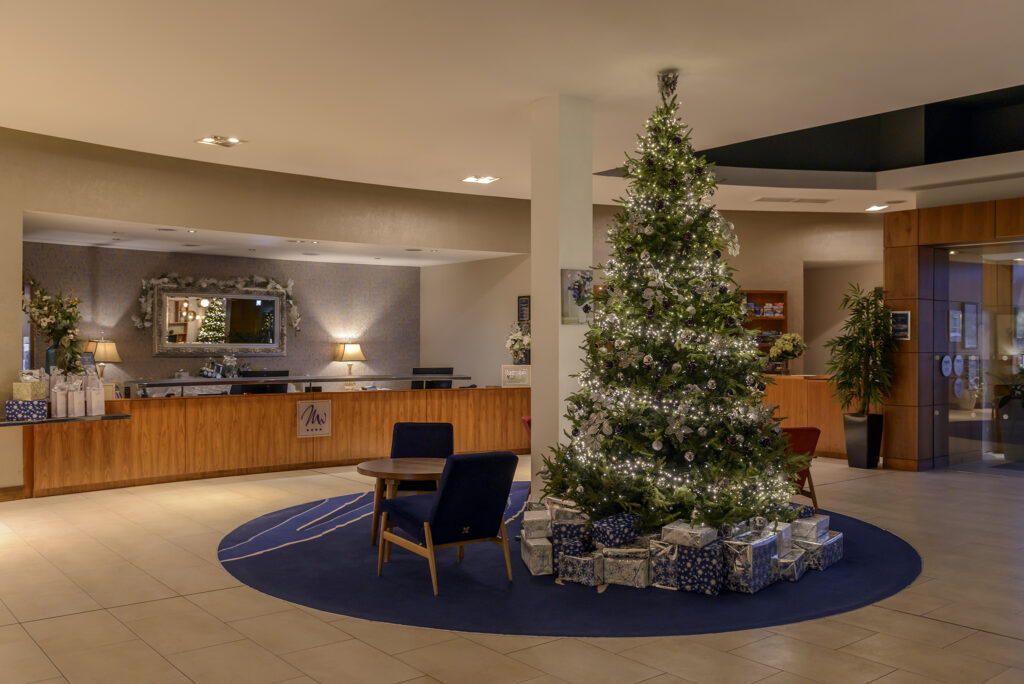 Christmas-Themed Hotel Lobby Festive hotel lobby with a sparkling Christmas tree, surrounded by presents, welcoming guests with warmth and elegance.
