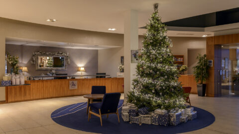 Festive hotel lobby with a sparkling Christmas tree, surrounded by presents, welcoming guests with warmth and elegance.