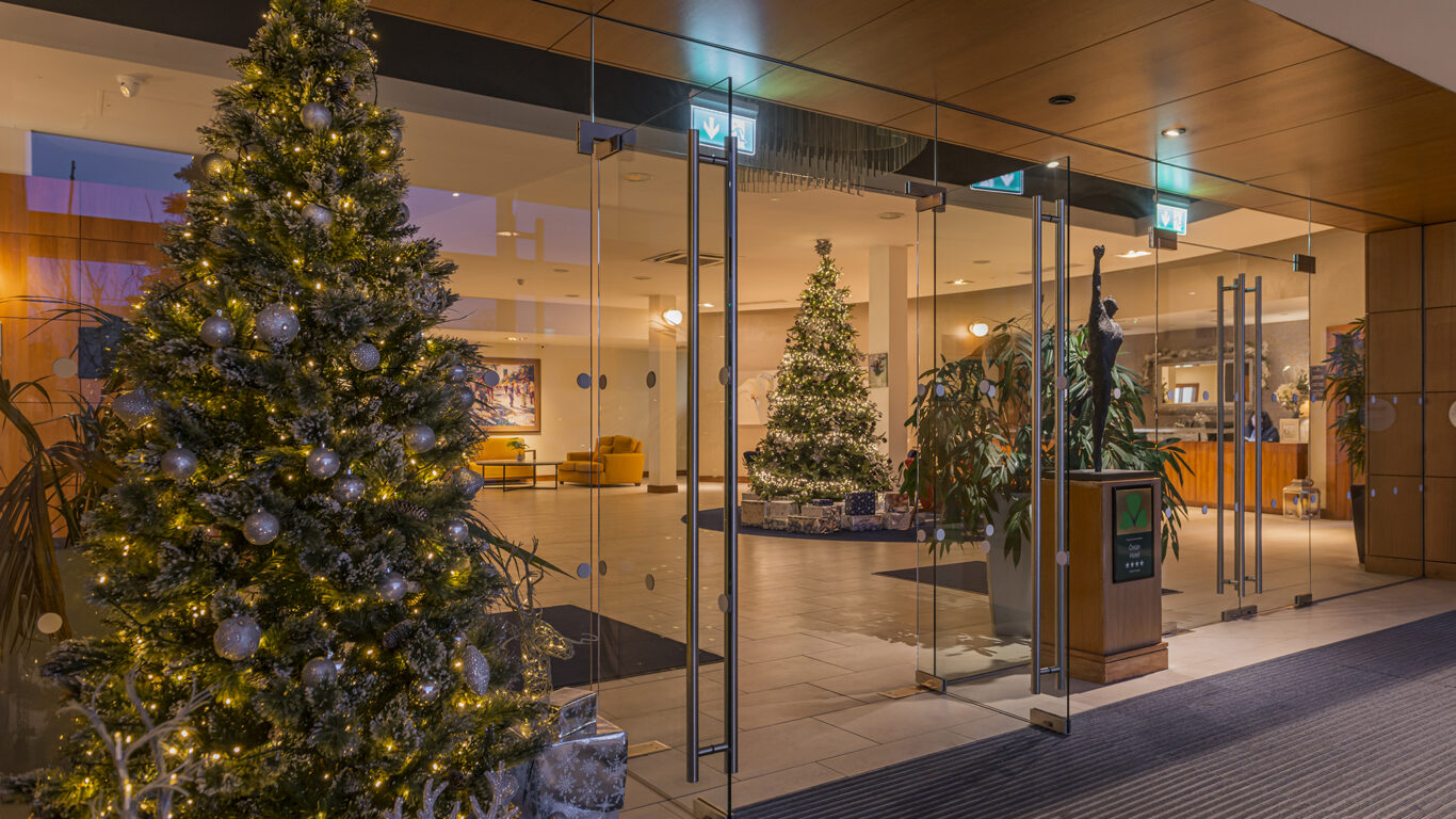 Festive hotel lobby with two illuminated Christmas trees, welcoming guests with a warm, elegant atmosphere.