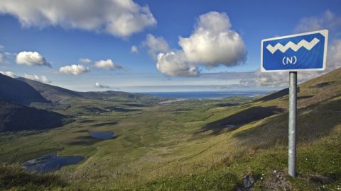 Panoramic view of lush green valley and distant ocean under blue sky, ideal for scenic drives and tranquil retreats.