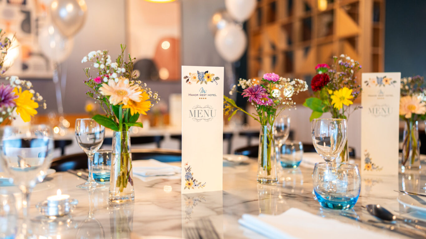 Elegant dining table with colourful flowers, wine glasses, and menu in a bright, welcoming hotel restaurant setting.