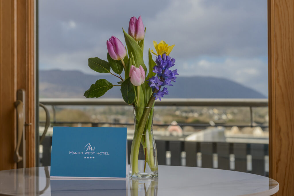 Scenic mountain view from hotel room, vibrant flowers and elegant card on table, welcoming ambience.
