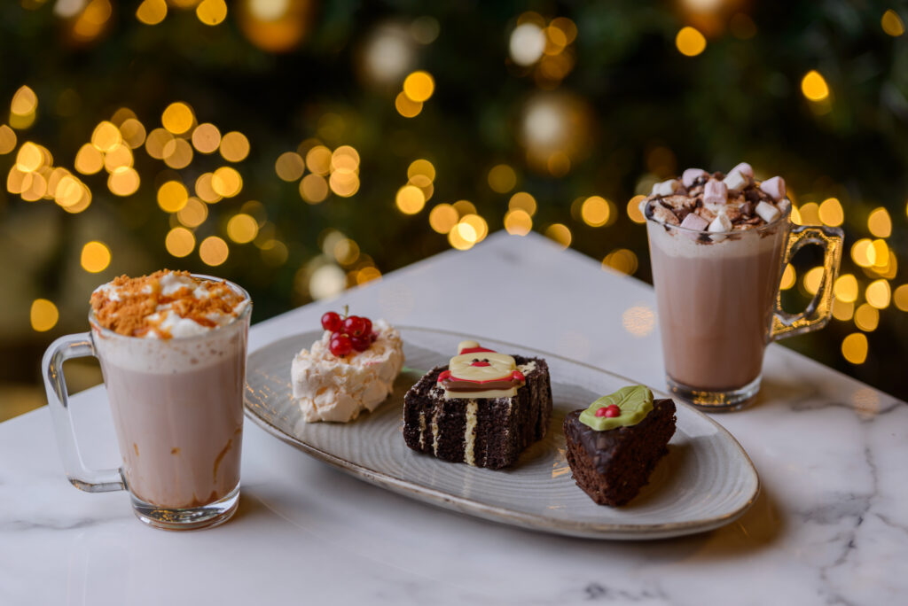 Festive Treats and Hot Chocolate Festive desserts with hot chocolate on a marble table, featuring Christmas lights, perfect for a cosy hotel stay.