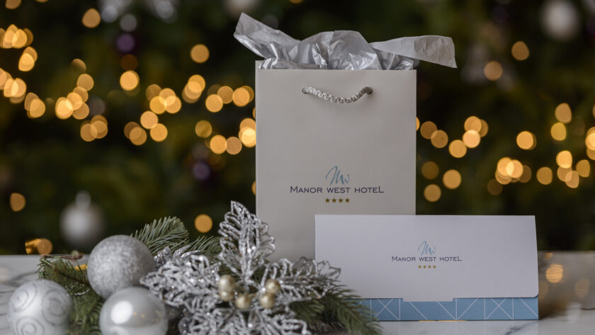 Elegant gift bag and invitation at Manor West Hotel, with festive lights and silver decorations, evoke a warm holiday welcome.